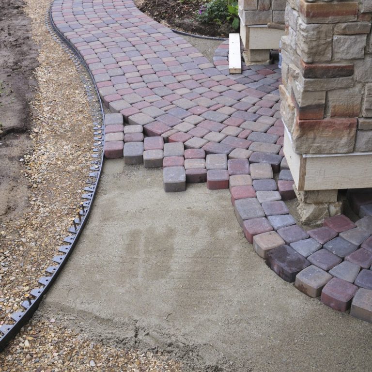 Brick walkway under construction beside a stone building, with gravel and soil base visible.